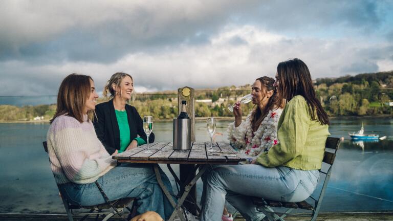 group of women drinking at outside table with dog at their feet and views of Menai.