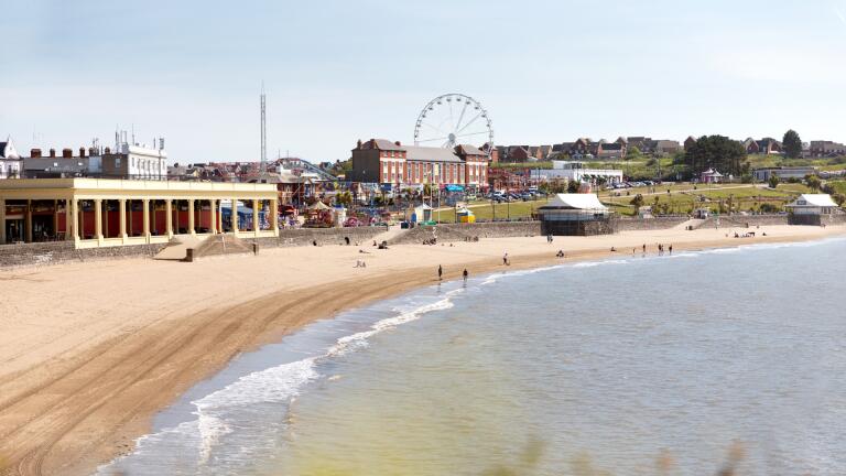 A wide sandy beach with a fairground in the background.
