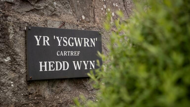 Arwydd leched gydag 'Yr Ysgwrn cartref Hedd Wyn' wedi ei ysgrifennu arno.