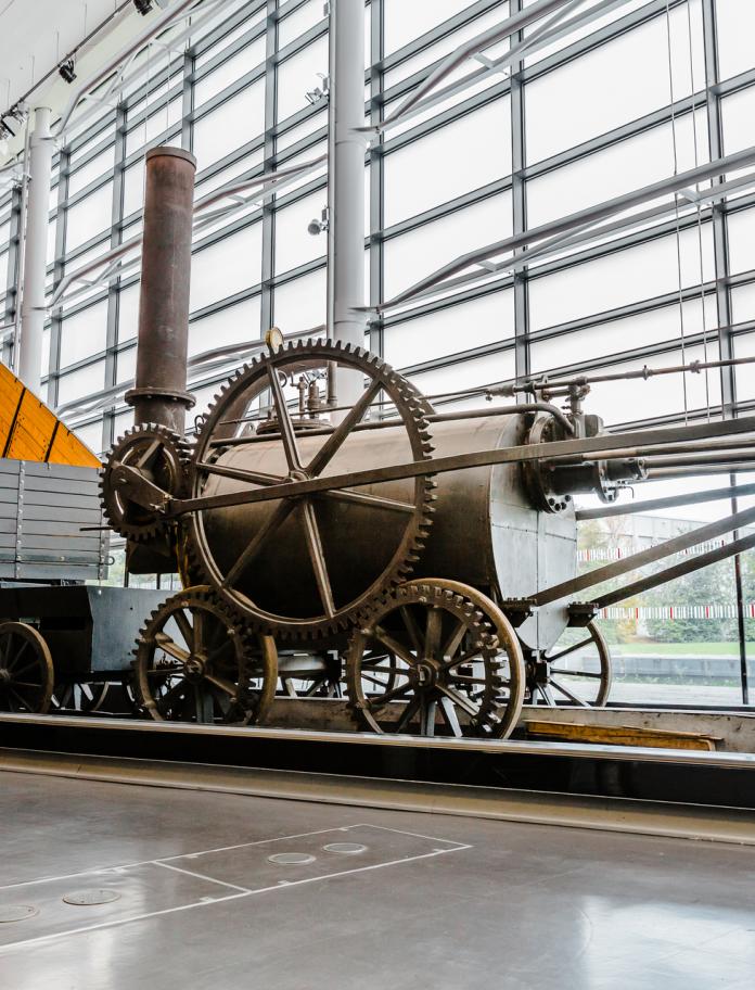 An industrial steam engine and wagon displayed in a window fronted museum.