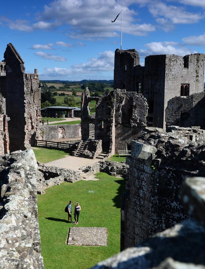 Raglan Castle from above, with two people walking through the ruins.