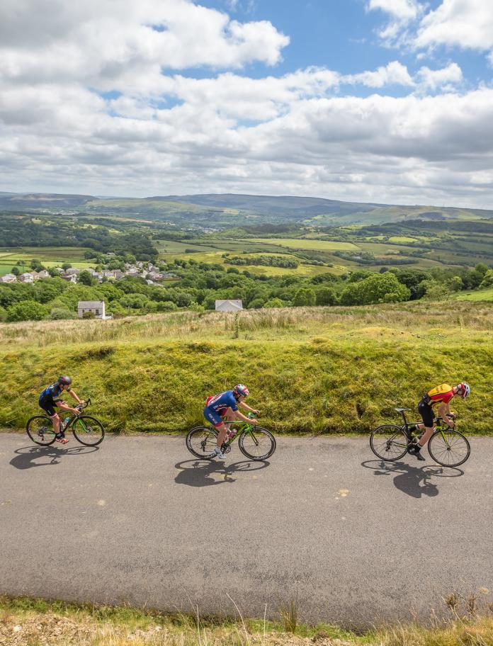 Three road cyclists cycling up a hilly road.