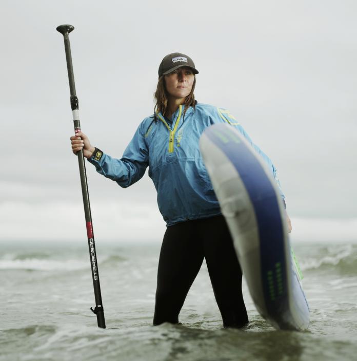 A woman standing in the sea holding a paddleboard.