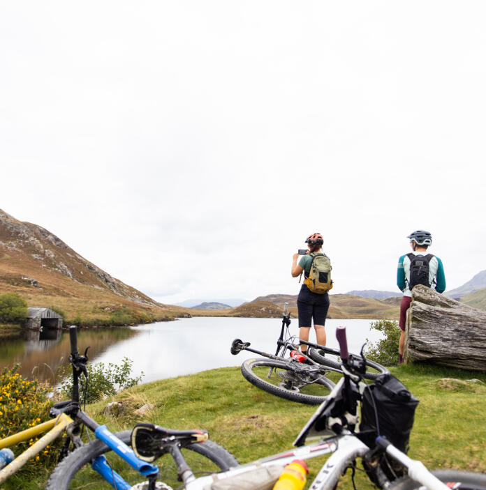 A group of mountain bikers resting by a mountainside lake.