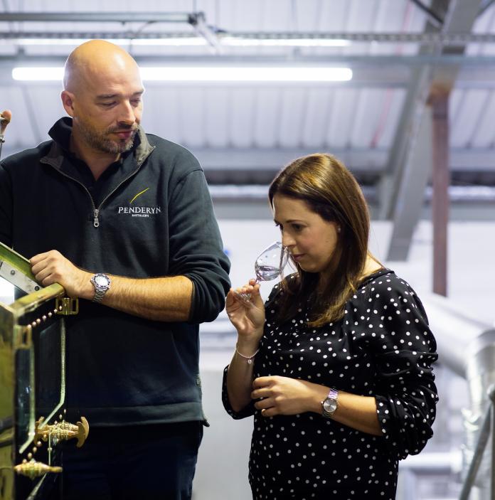 Laura Davies sniffing a glass inside the Penderyn distillery with a colleague.