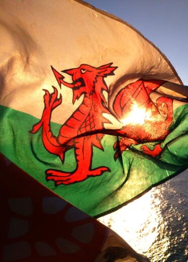 Die walisische Flagge flattert im Sonnenuntergang mit dem Meer im Hintergrund.