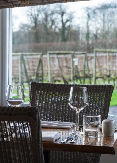 Ein eingedeckter Tisch im Restaurant vor einem Fenster mit den Weinstöcken im Hintergrund.  a vineyard.