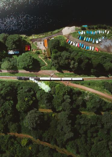 Luftaufnahme einer Dampfeisenbahn der Brecon Mountain Railway, die an einem Fluss entlangfährt.