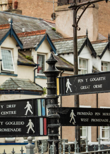 Welsh and English direction signs from a town centre.