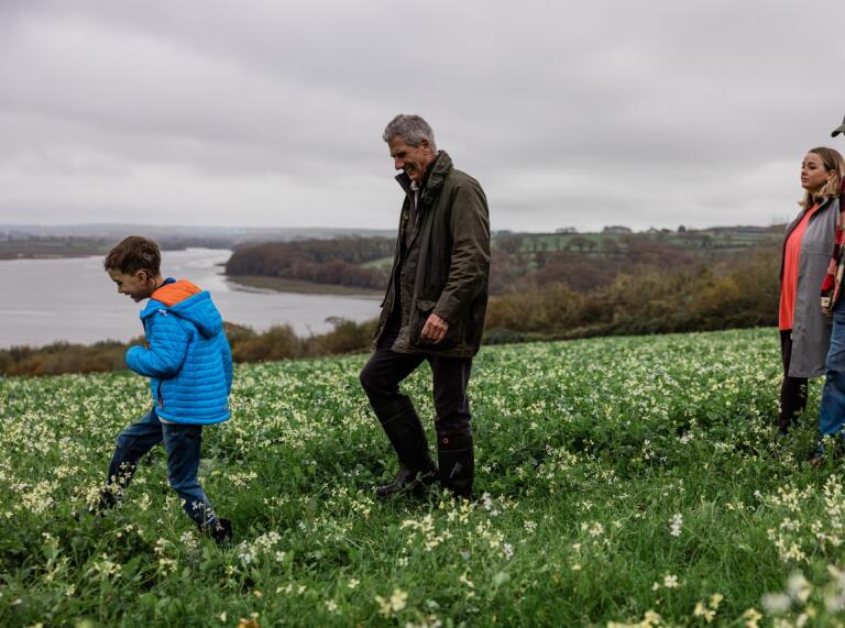 Drei Erwachsene mit einem Jungen spazieren durch ein Feld in Lawrenny, mit Blick auf die Mündung des Flusses Cleddau.