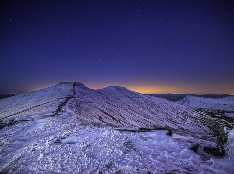 View of stars in the dark sky and snow-covered mountains in the foreground