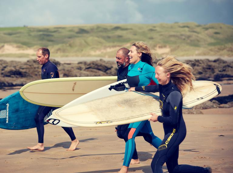 Vier Surfer die den Strand mit ihren Bretten hinunterrennen.