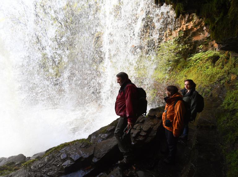 Family walking behind Sgwd yr Eira waterfall