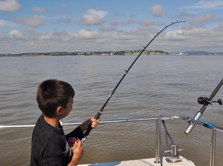 A boy with a fishing rod off the side of a boat.