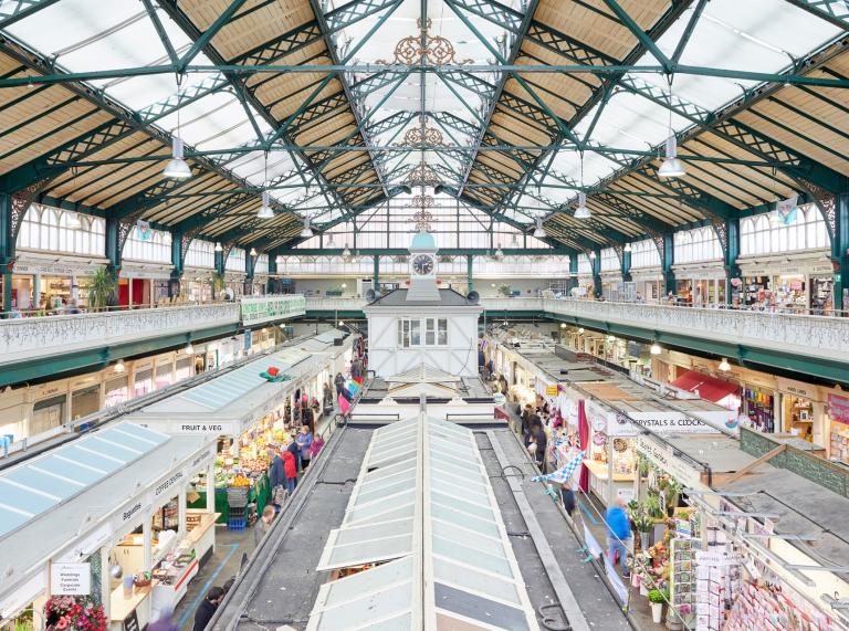 An indoor market under a triangular roof with skylights. There are lots of different stalls in rows.
