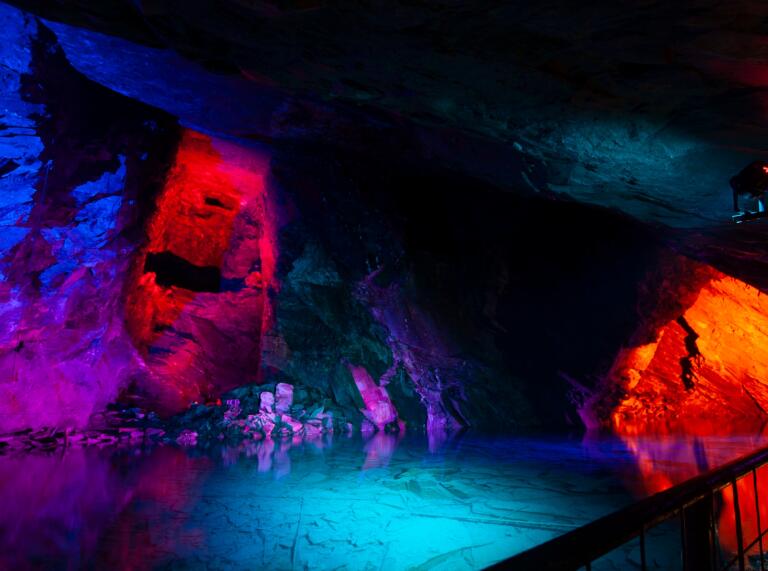 Schieferhöhle mit einer natürlichen Quelle in bunten Farben erleuchtet.
