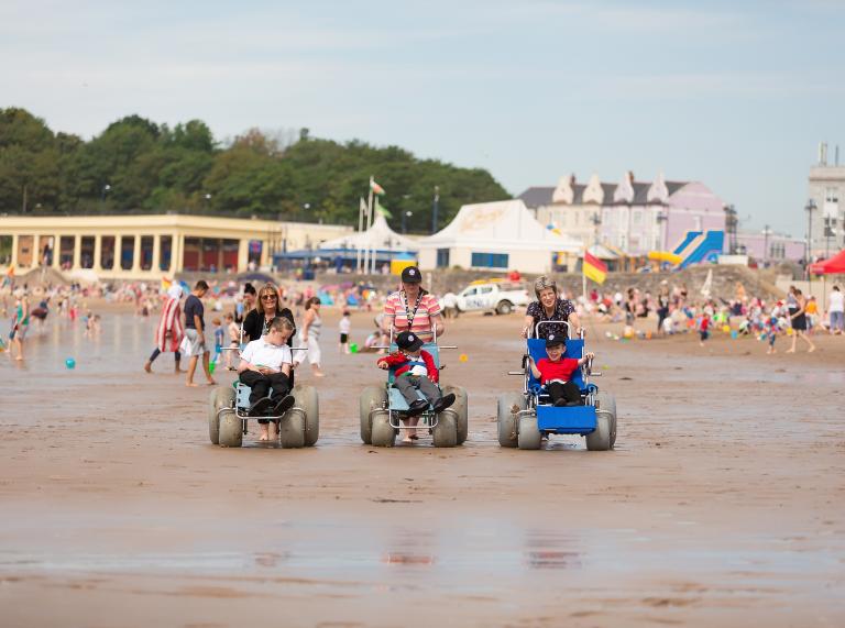 Three people using beach wheelchairs at Whitmore Bay beach.