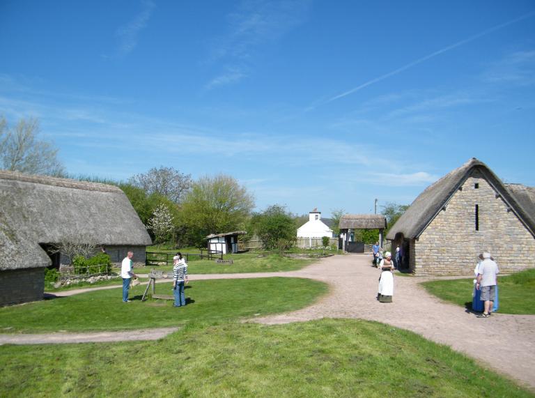 Exterior of thatched buildings in Cosmeston Village, with people walking around.