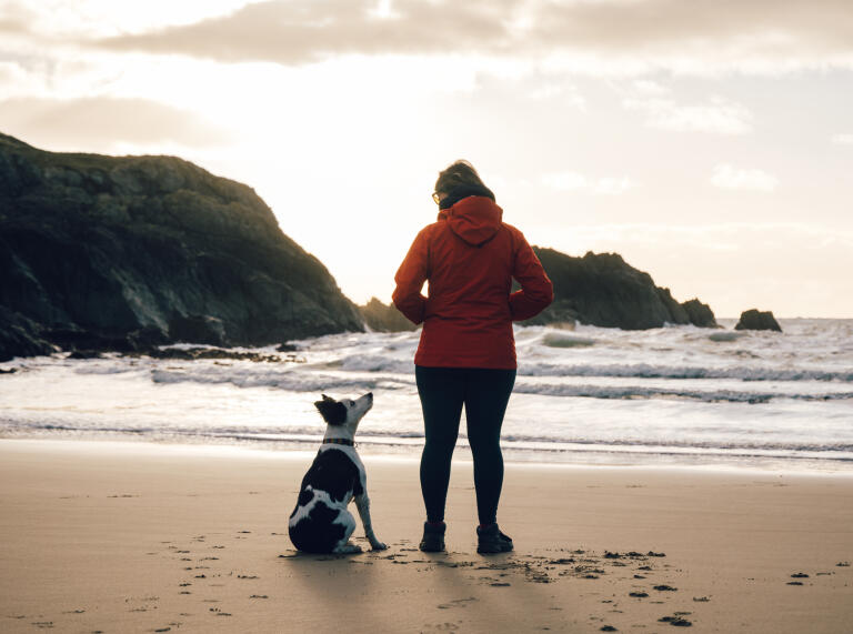 woman and dog on sandy beach.