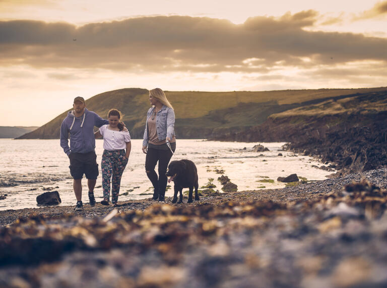 Eine Familie, die mit ihrem Hund am Strand von Manorbier spazieren geht.
