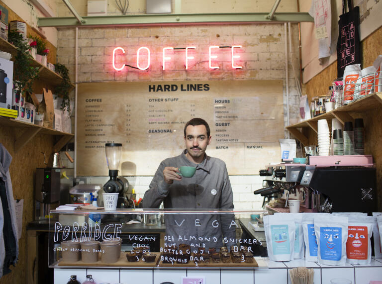 A man standing behind a counter holding up a cup of coffee.
