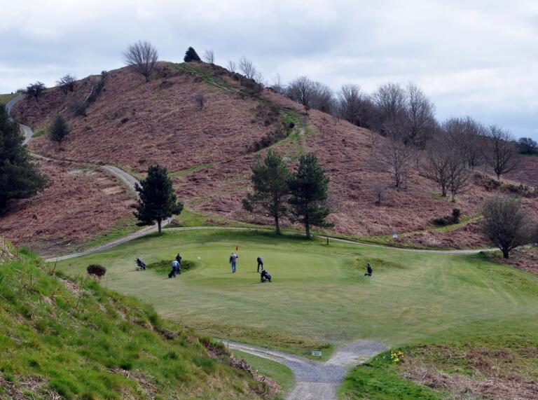 people playing golf on course with hill.