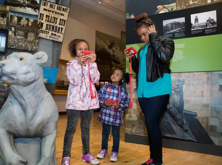 Three children using hand held audio visual guides at a museum