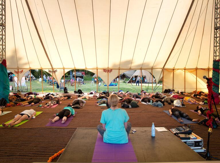 People practicing yoga in a large tent at a festival