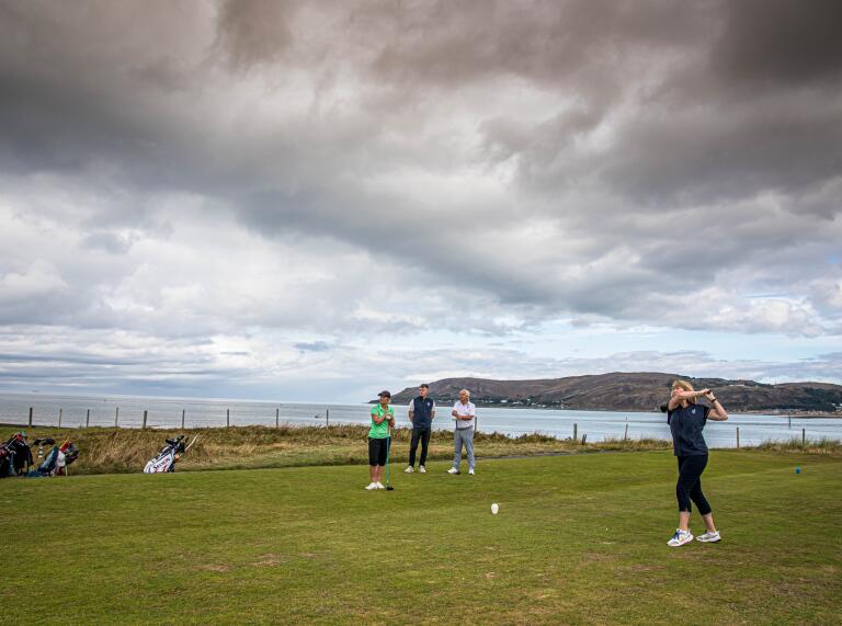 A group of people playing golf at a coastal golf course.