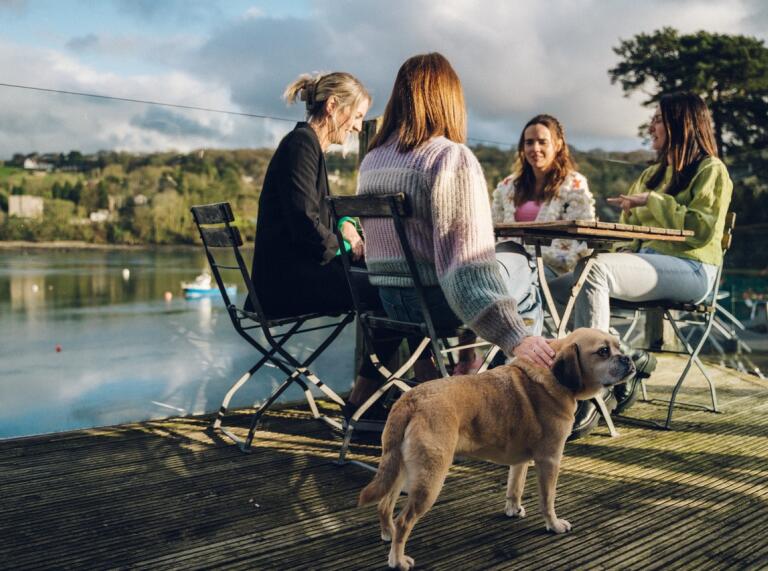 group of women drinking at outside table with dog at their feet and views of the Menai Straits.
