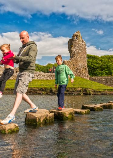 Family walking across stepping stones over Ogmore River.