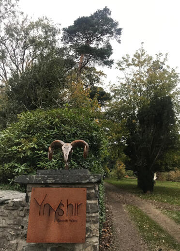 A rusted 'Ynyshir' sign on a gate pillar, with a horned skull on top.