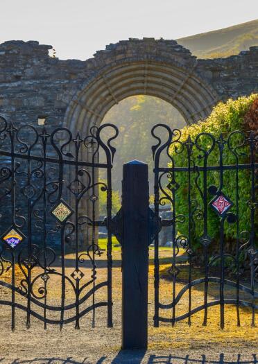 Iron wrought gates embellished with Celtic symbols with the doorway to abbey beyond. ruined a