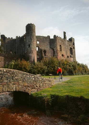 A cyclist riding by a ruined castle.