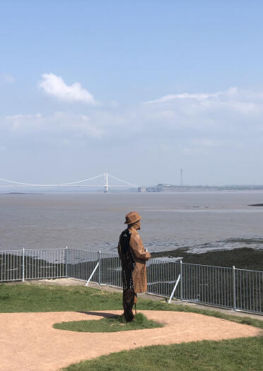 A tall metal sculpture of a man looking out over an estuary.