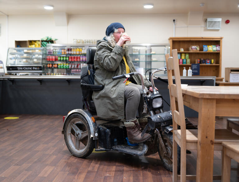 A lady sat on a mobility scooter having a drink in a cafe.