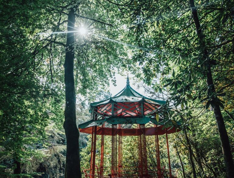 An ornate red and green painted pagoda in woodland.