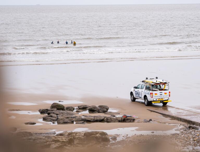 An RNLI car on a sandy beach, with surfers in the sea.
