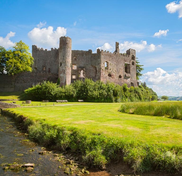 Ruined castle on a sunny summer day with stream and grassy bank in the foreground