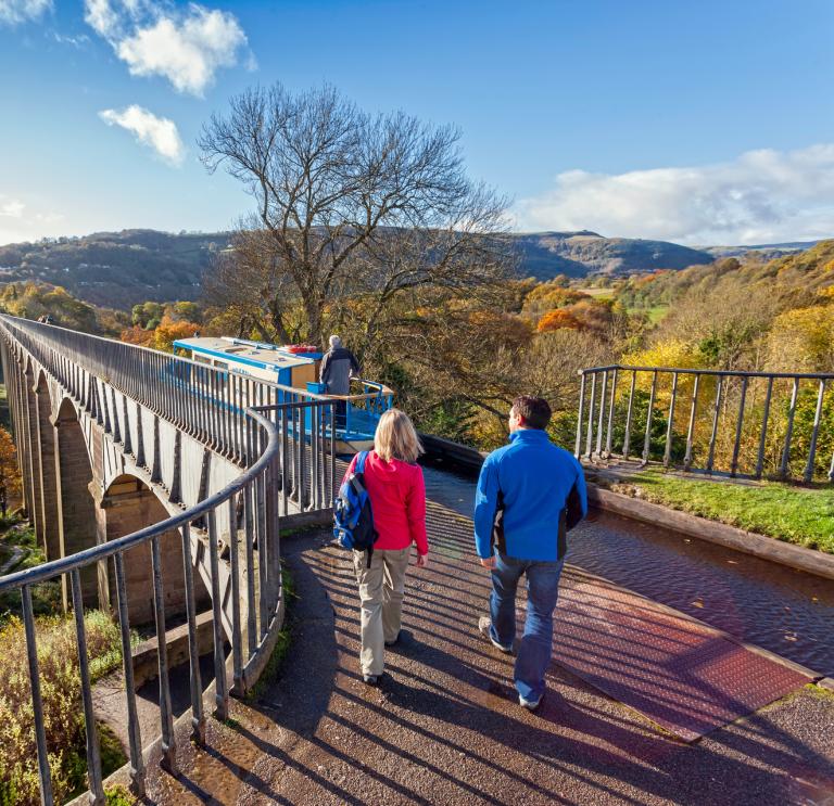 Blick auf zwei Personen, die auf dem Pontcysyllte-Aquädukt im Herbst spazieren gehen.