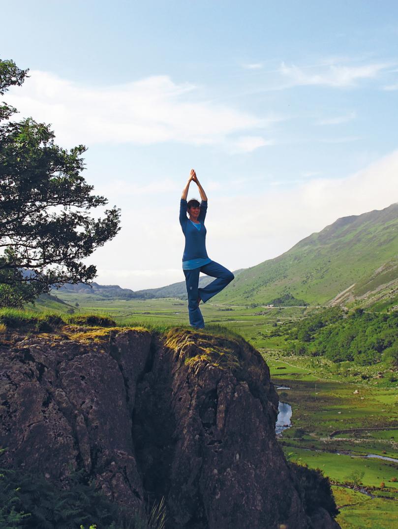 Bild einer Frau, die Yoga auf einem Felsvorsprung macht.