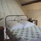 Traditional Welsh black iron bed with patterned green and white Welsh tapestry bed sheet.