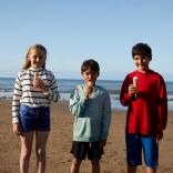 Three children standing on a beach on a sunny day eating ice cream 