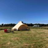 A glamping tent in a grass field on a sunny day.