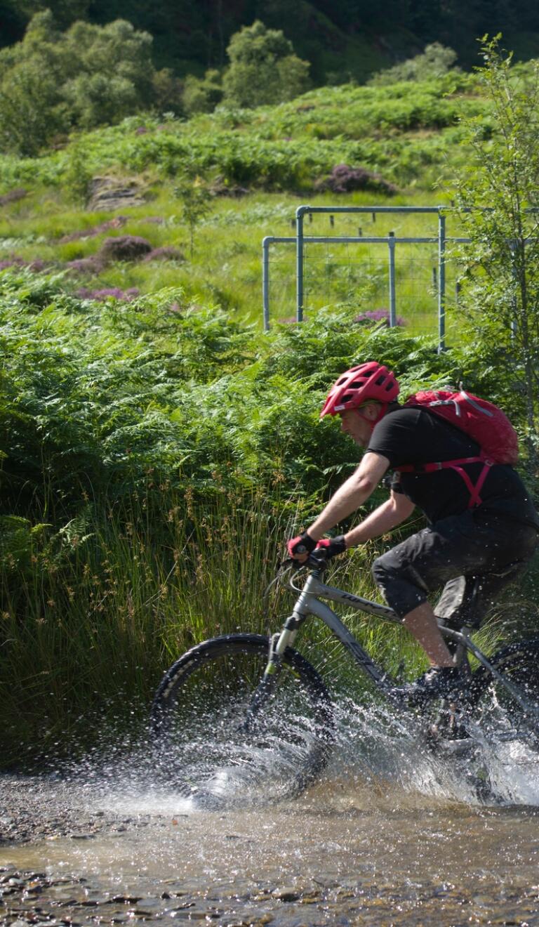 A mountain biker cutting through a river in Ceredigion. 