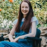 woman with long brown hair smiling as she's sat in chair in garden.