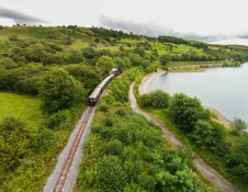 A narrow gauge steam hauled train next to a reservoir.