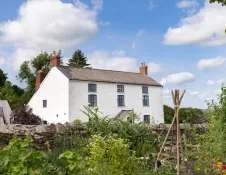 A large, white-washed cottage next to a flower garden. 