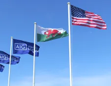 Row of AIG Women’s Open flags with Welsh dragon flag and U.S. stars and stripes waving in bright daylight.