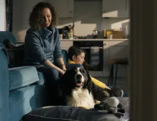 Adult and child sitting on a sofa in a cosy living room with a relaxed black and white dog lying in front of them.